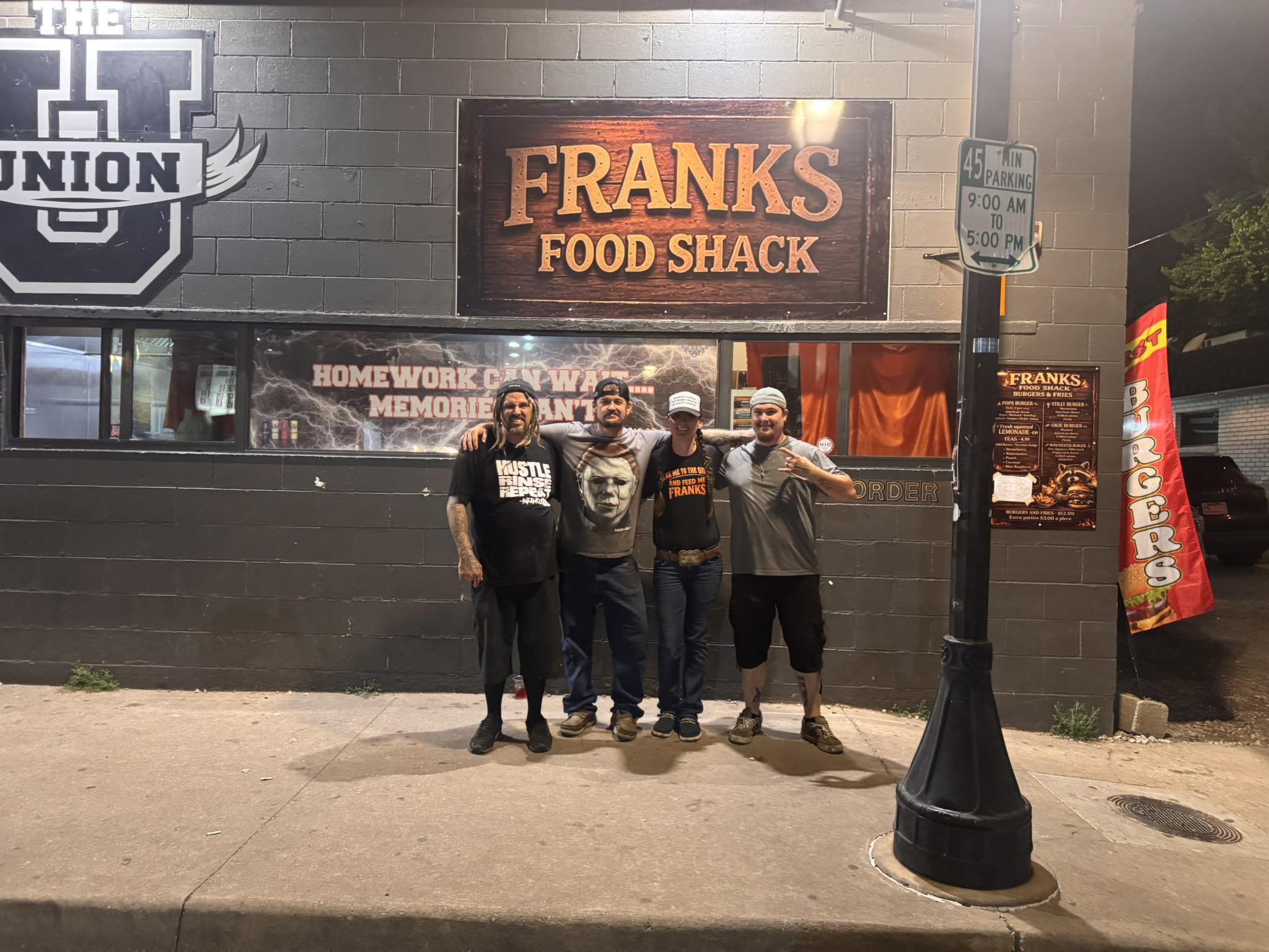 Frank's Food Shack at night: wooden sign, team in front of the brick building on the strip